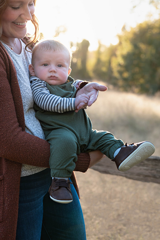 Mother smiles while looking down at her baby during family portrait shoot