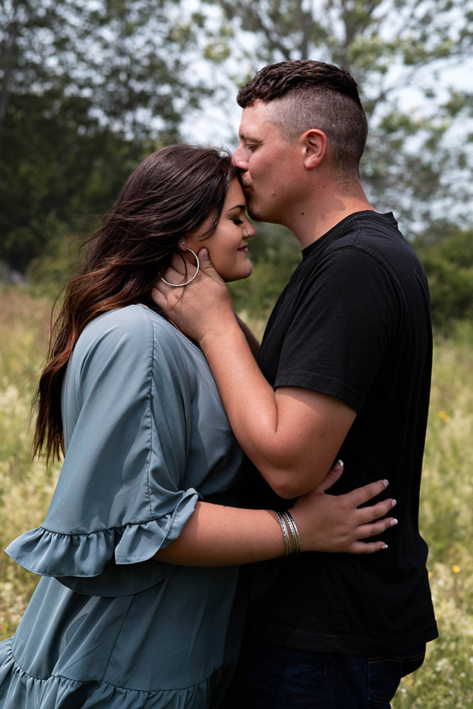 Woman getting kissed on the forehead by her fiancé during their engagement shoot