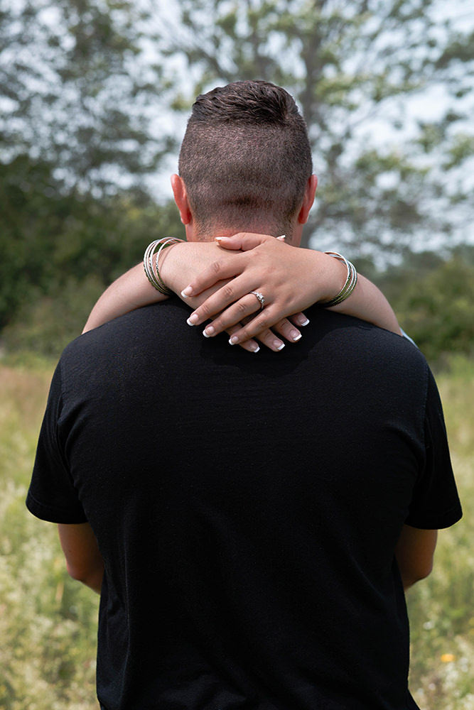 Woman's hands wrap around back of neck of her fiancé during their engagement shoot