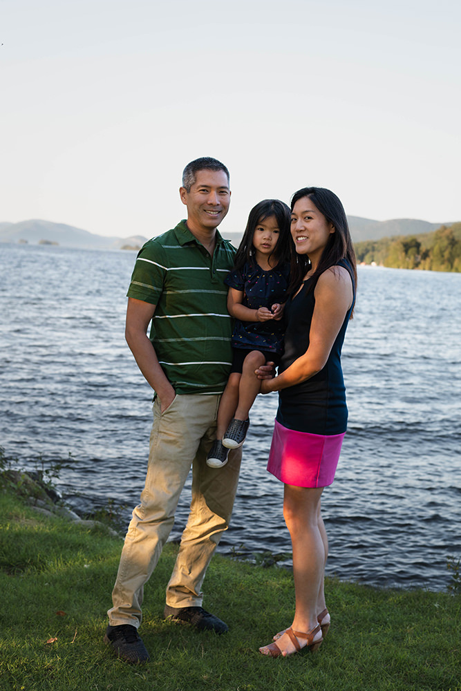 Family stand in front of lake with mother holding daughter